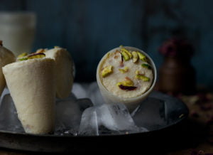 Traditional cone-shaped Malai Kulfi served on a plate with a sprinkle of cardamom powder