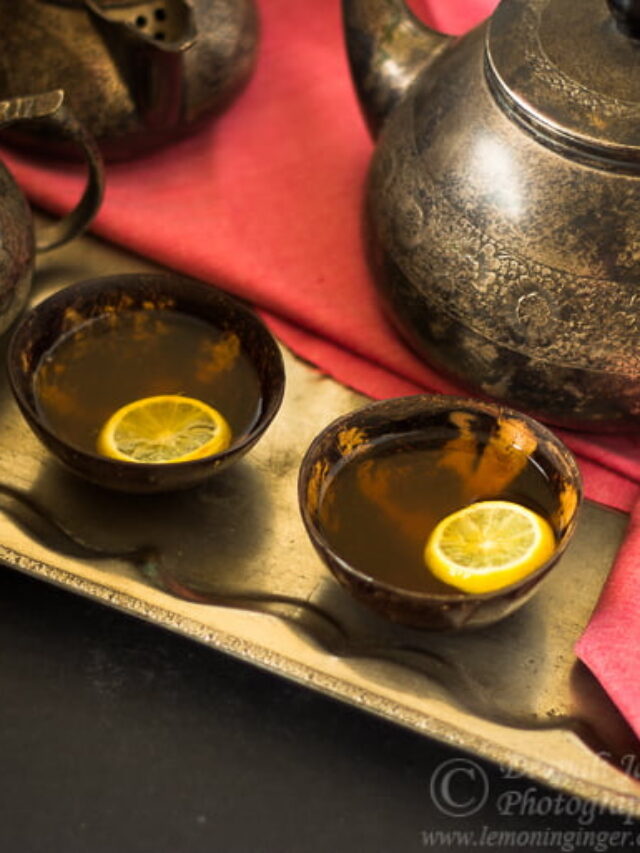 Two glasses filled with hot lemon tea with a teapot
