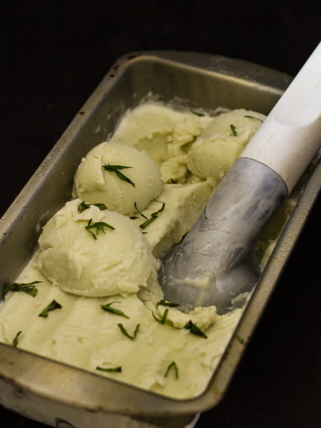 Several scoops of basil ice cream in a ice cream tray, with fresh basil leaves on the top