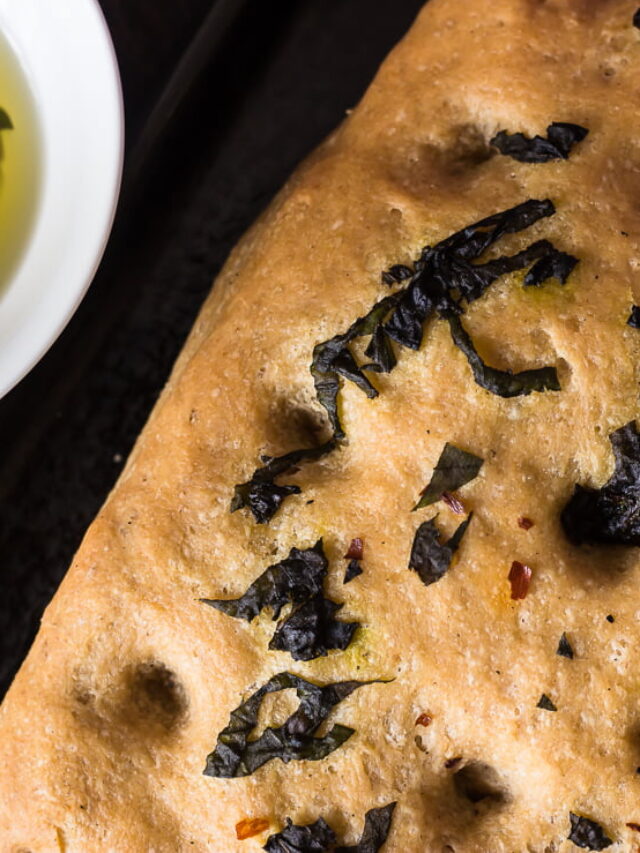 Close-up of golden crust and basil topping on whole wheat focaccia bread