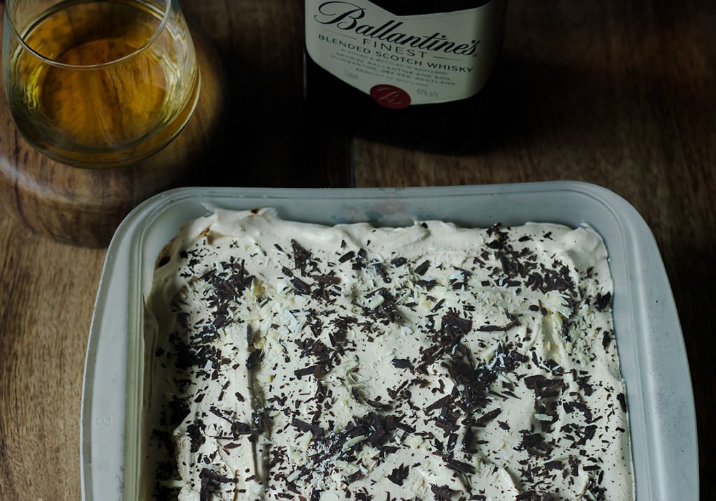 Eggless Whiskey Coffee Poke Cake topped with whipped cream and chocolate curls