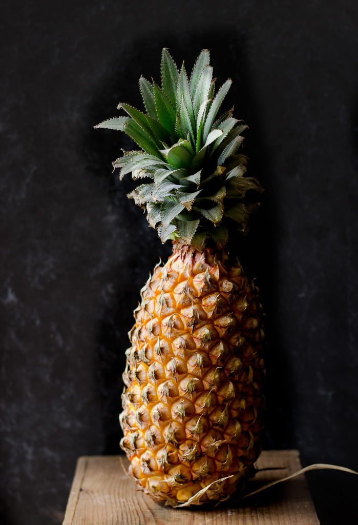 A whole pineapple with its spiky green crown and textured golden skin