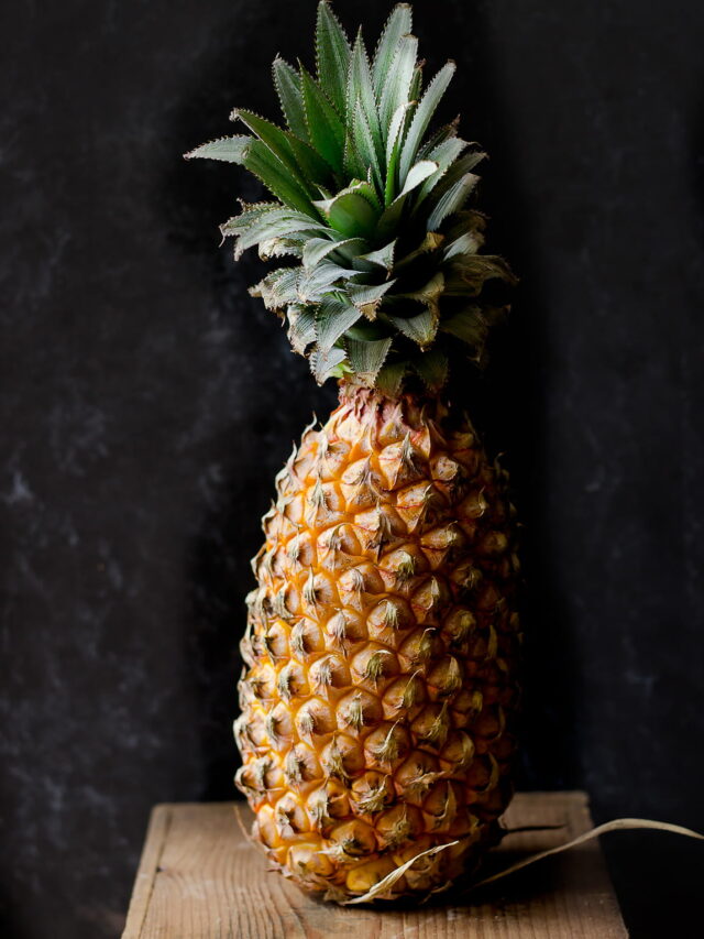 A whole pineapple with its spiky green crown and textured golden skin