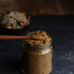 A spoonful of homemade garam masala stored in a jar, showing its rich texture and color