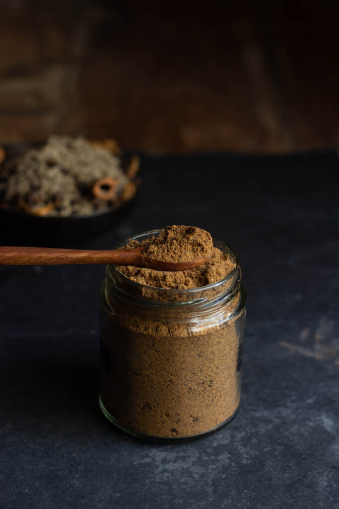 A spoonful of homemade garam masala stored in a jar, showing its rich texture and color