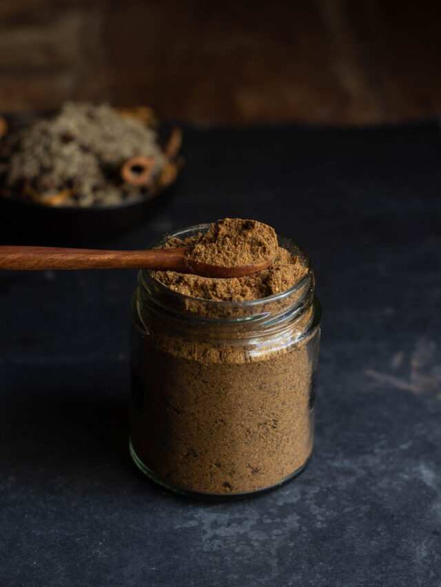 A spoonful of homemade garam masala stored in a jar, showing its rich texture and color