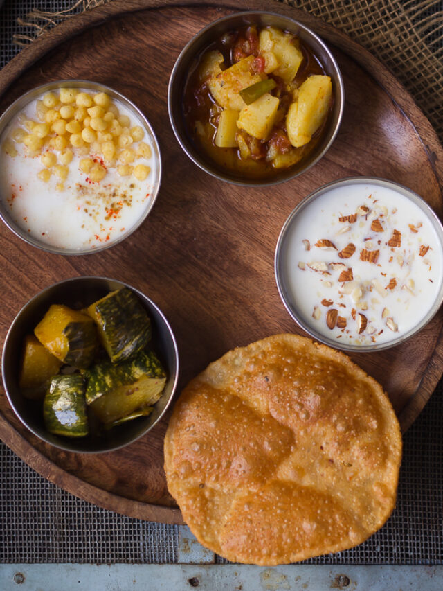 A plate of puris, golden and puffed, alongside a bowl of raita on the Satvik Thali